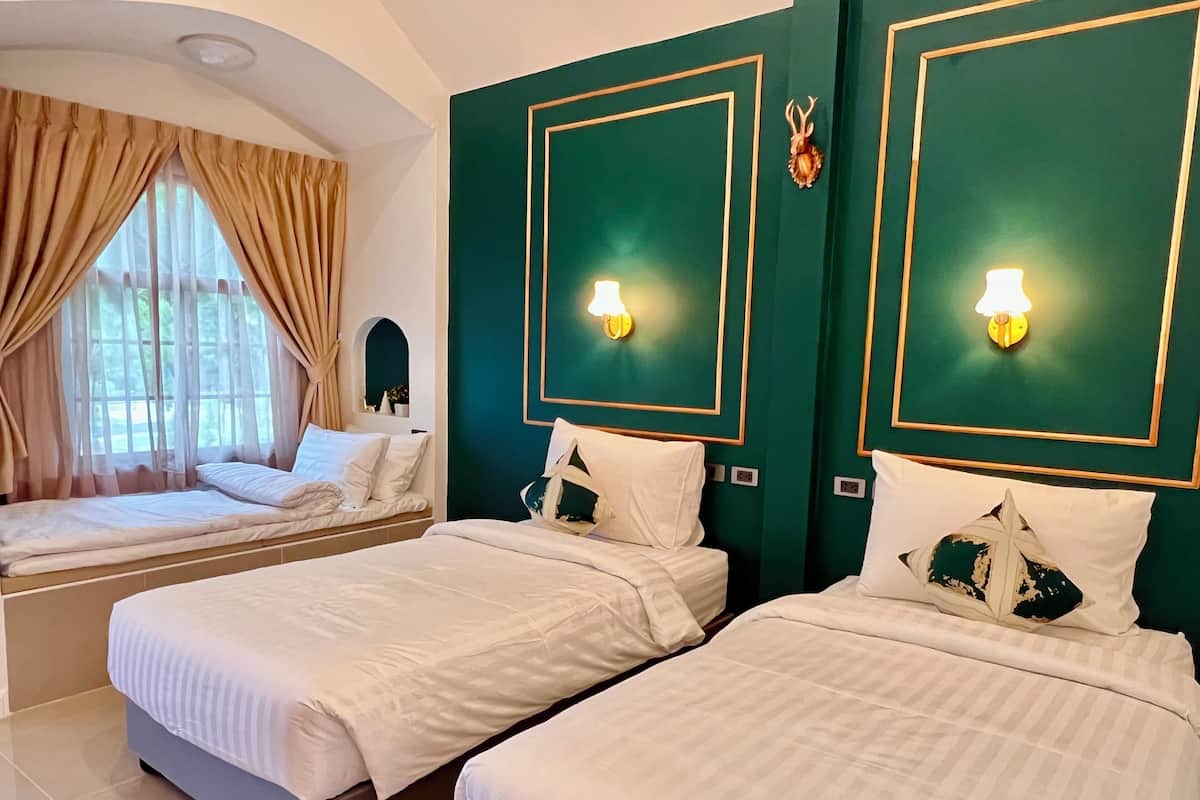 Quarto de hotel com duas camas, cortinas bege, uma parede de destaque verde e luminárias fixadas na parede.
