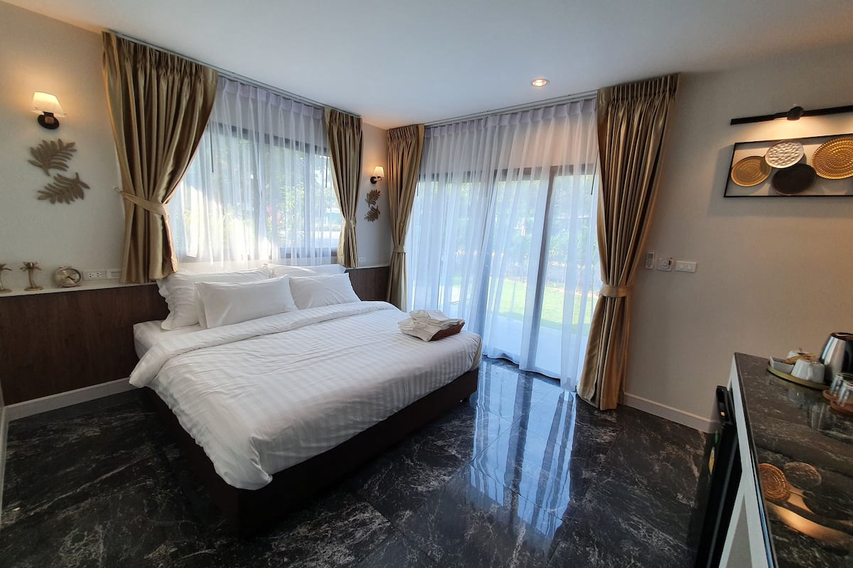 Quarto de hotel moderno com uma cama grande, piso de mármore escuro e cortinas leves.