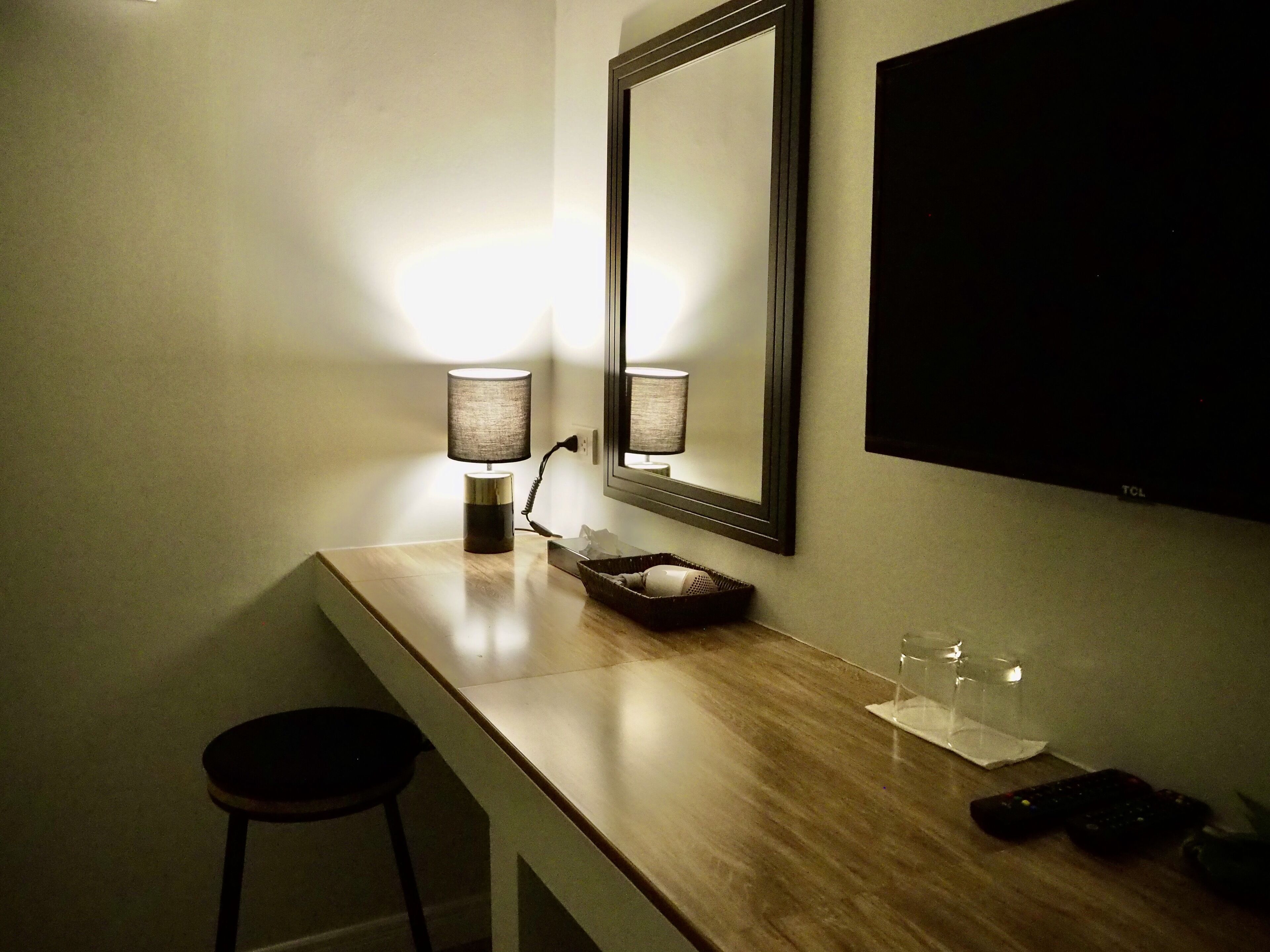 Una habitación de hotel con un escritorio de madera, dos lámparas, un espejo, un televisor y un control remoto.