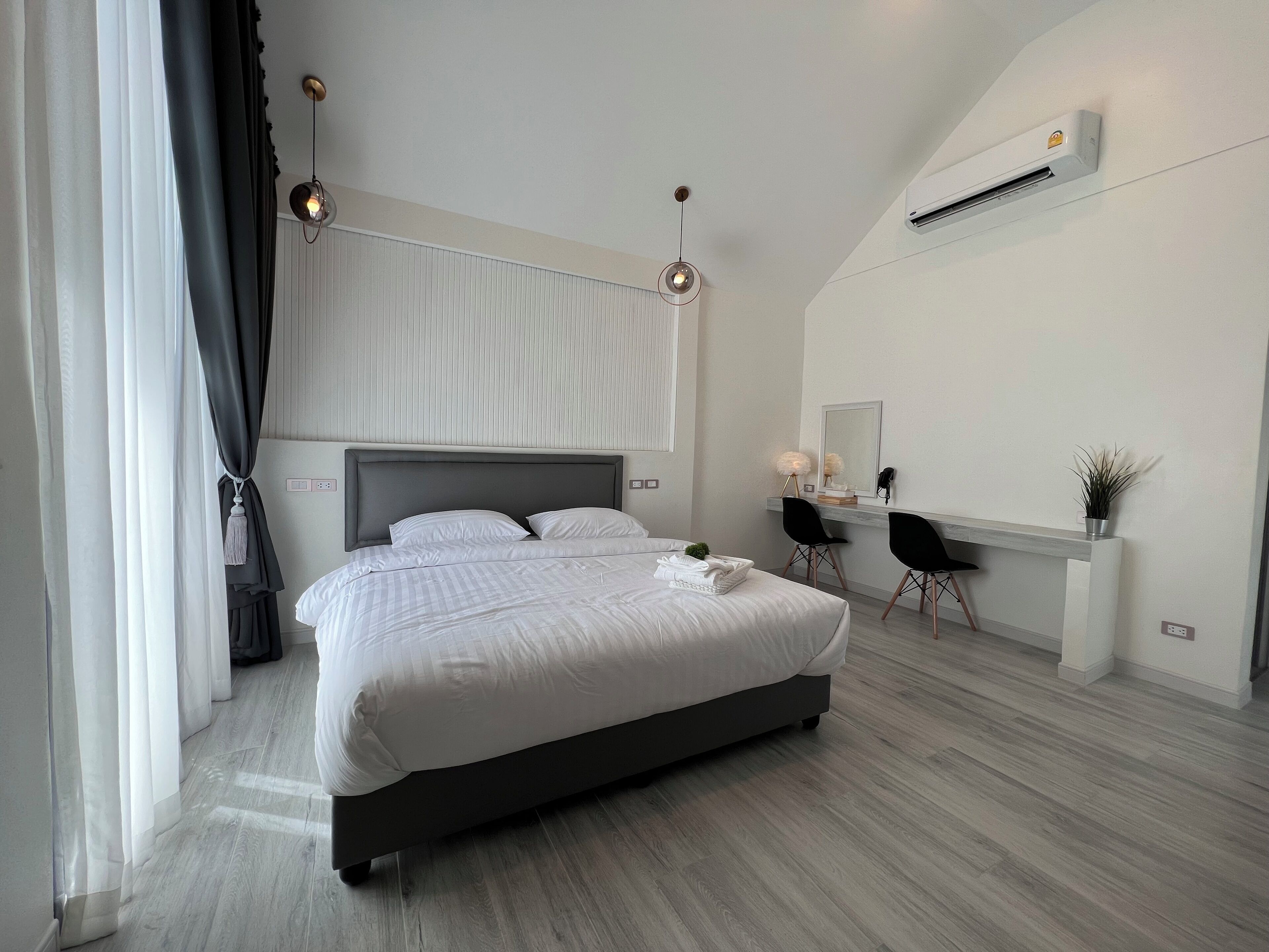 Un dormitorio moderno con una cama grande, un escritorio con dos sillas, un espejo y un equipo de aire acondicionado.