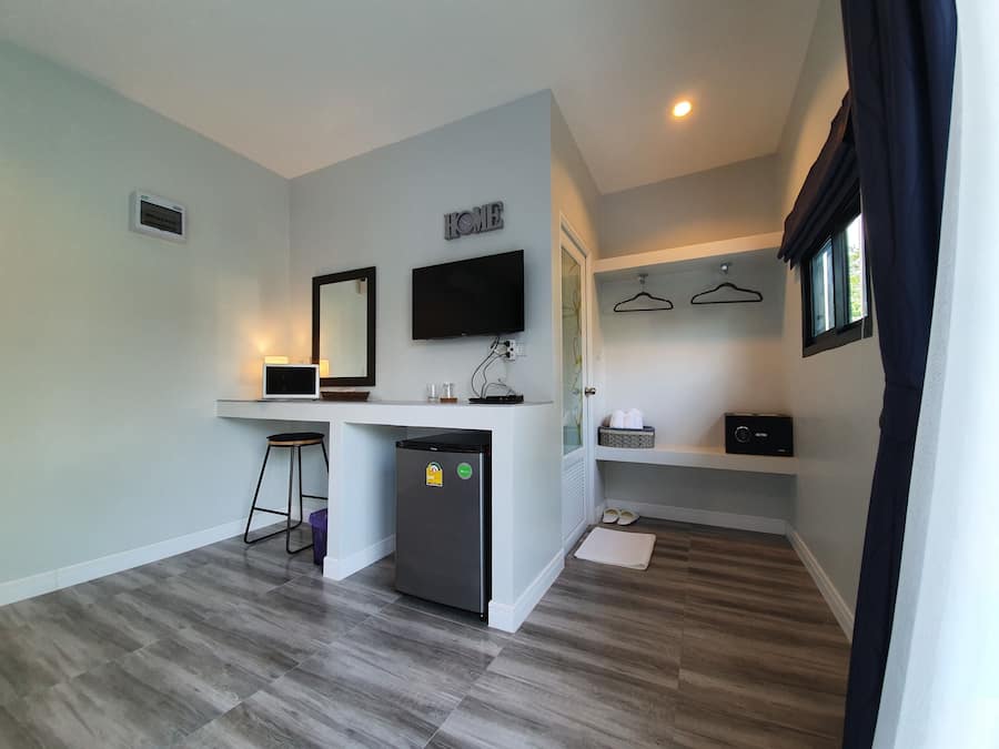 Een moderne hotelkamer met een kitchenette, een flatscreen televisie, een spiegel, een kleine koelkast en een zithoek met een kruk.