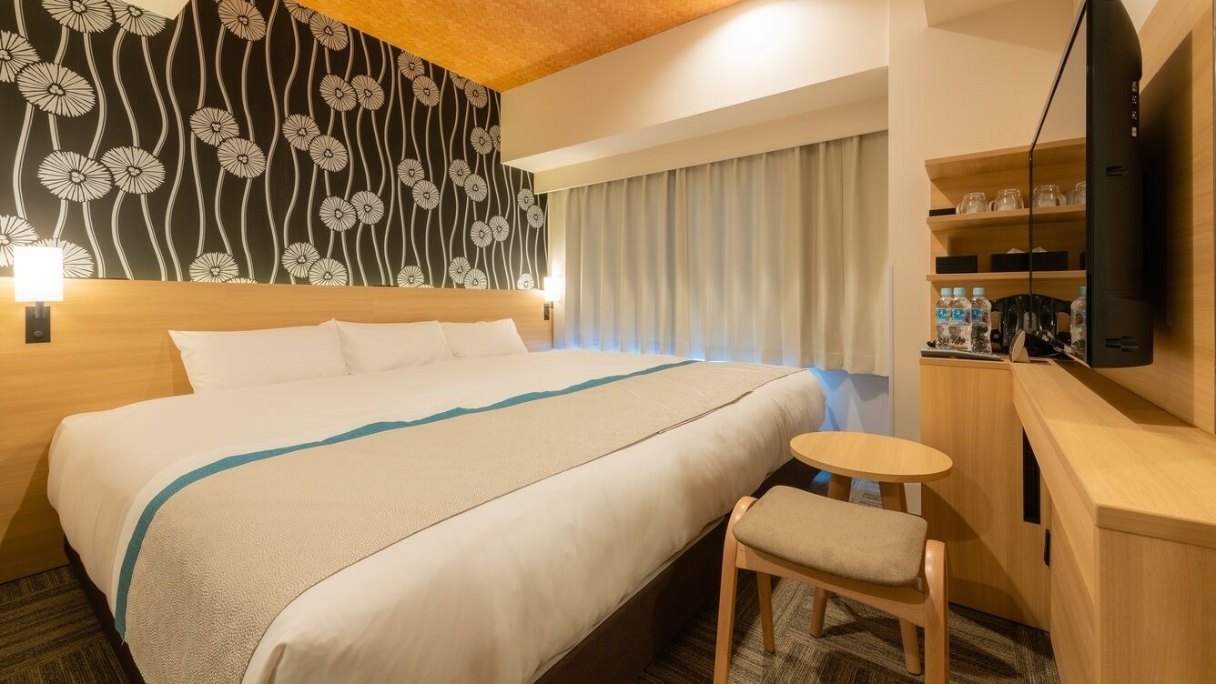 A hotel room with a bed, a small table, a TV, and a wall with a floral pattern.