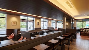 A modern restaurant with high tables and booths, large windows, and a brick accent wall.