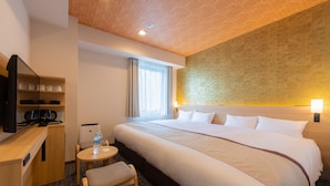 A hotel room with a large bed, a desk with a chair, a television, and a small table with a water bottle.