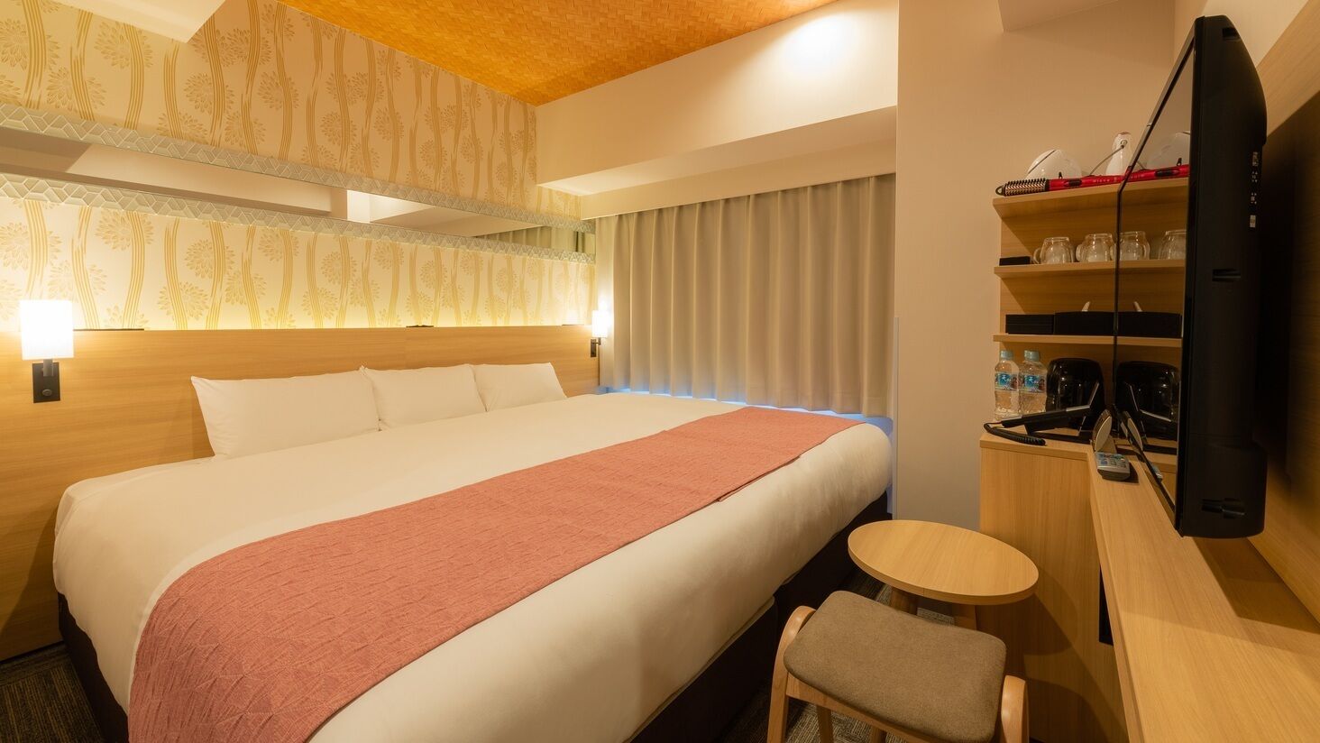 A hotel room with a large bed, a desk with a chair, a television, and a minibar.