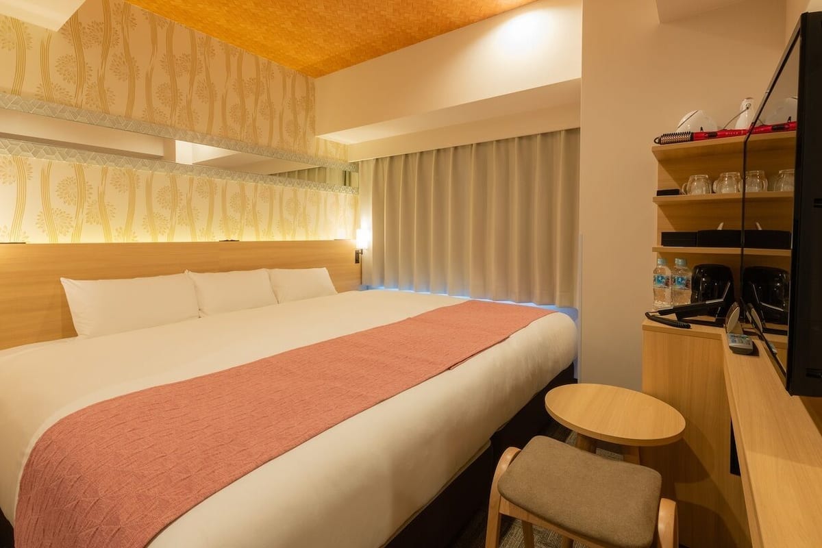 Ein Hotelzimmer mit einem großen Bett, einem Schreibtisch mit Stuhl, einem Fernseher und einer Minibar.