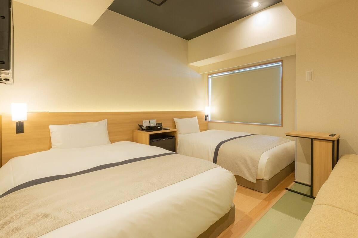 A hotel room with two beds, a desk, a chair, and a large window.