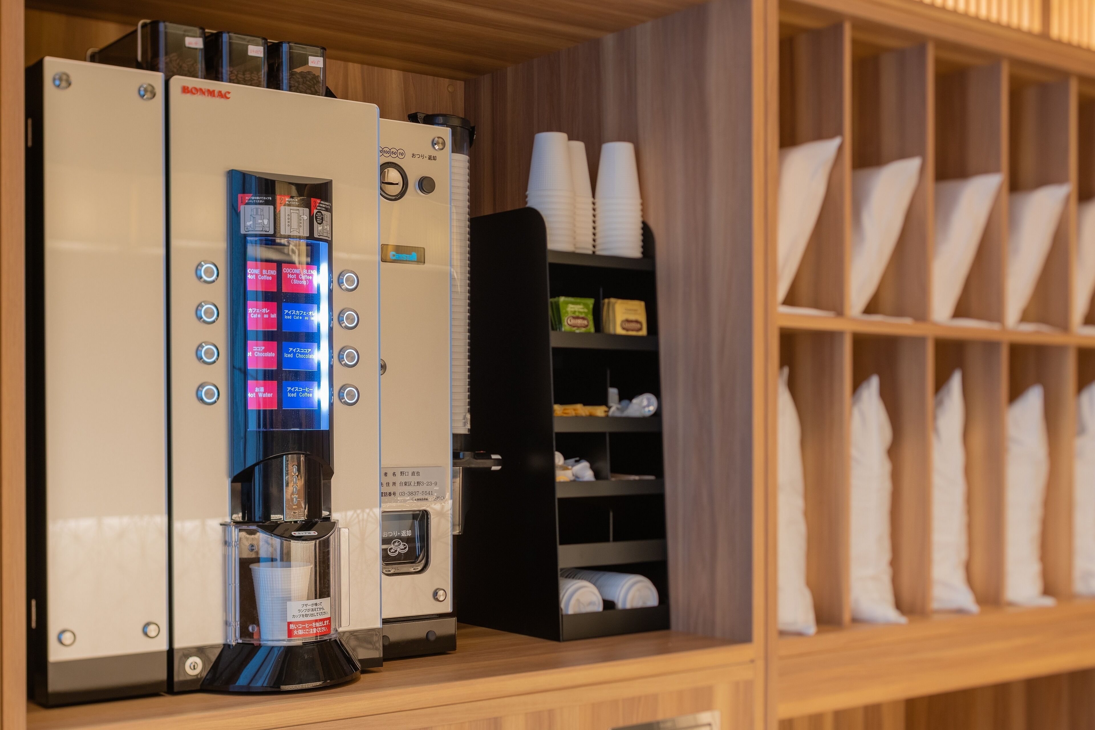 A coffee machine with a digital interface, a shelf with stacked cups, and a storage unit with folded towels.