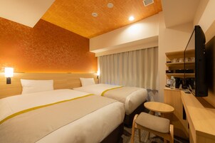 Une chambre d’hôtel avec deux lits, un bureau, une chaise, une télévision et une fenêtre avec des rideaux.