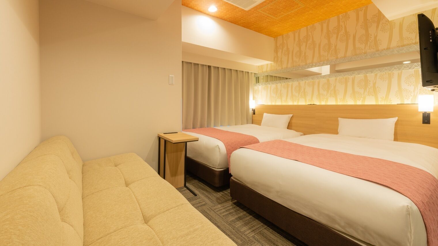 A hotel room with two beds, a sofa, a small table, and a television.