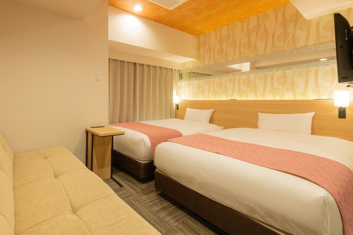 Ein Hotelzimmer mit zwei Betten, einem Schlafsofa, einem kleinen Tisch und einem Fernseher.