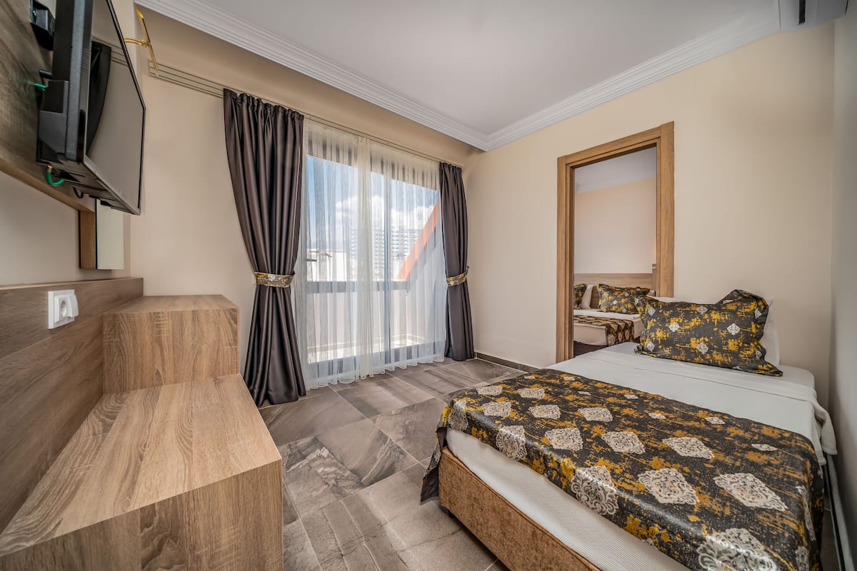 A hotel room with a bed, a TV mounted on the wall, a desk, and a large window with curtains.