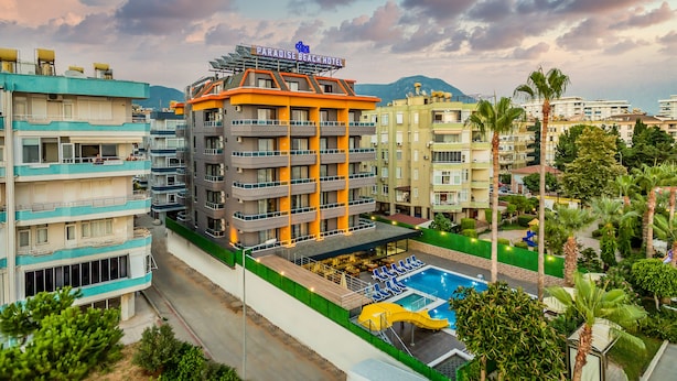 A multi-story hotel with a swimming pool, outdoor seating, and a mountain backdrop. - Arsi Paradise Beach Hotel (Alanya)