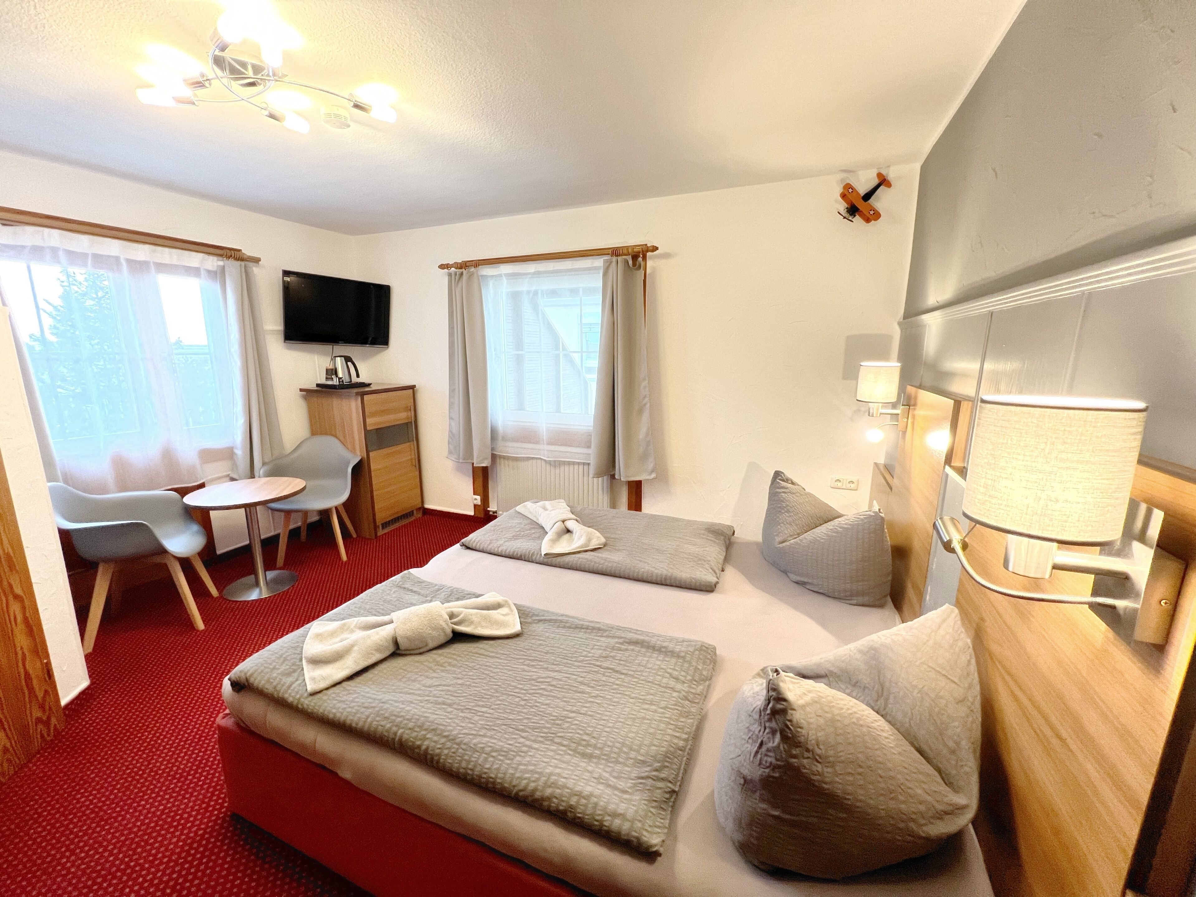 Hotelkamer met een bed, twee kussens, een nachtkastje met een lamp, een bureau met stoel, een televisie en een raam met gordijnen.