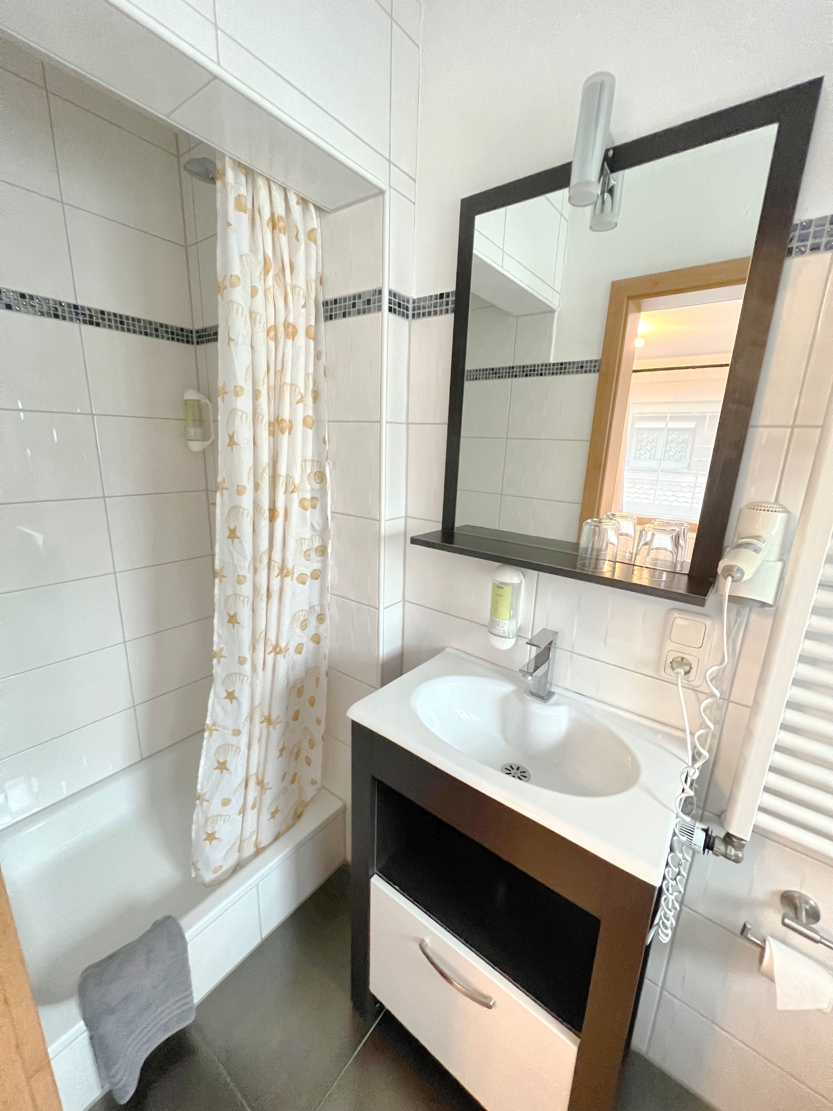 Un baño con bañera, lavamanos con espejo y un perchero para toallas.