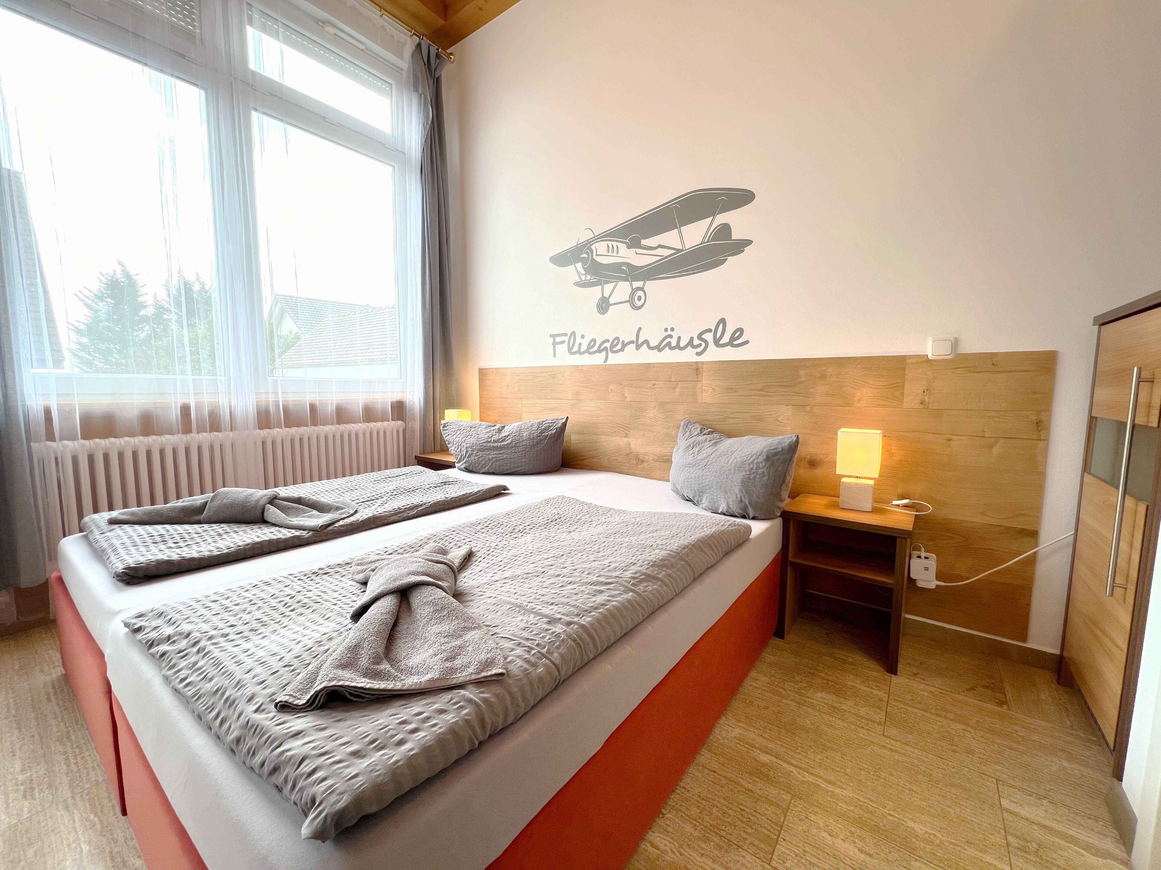 A hotel room with two beds, a wooden headboard, a wall-mounted airplane decal, and a window with sheer curtains.