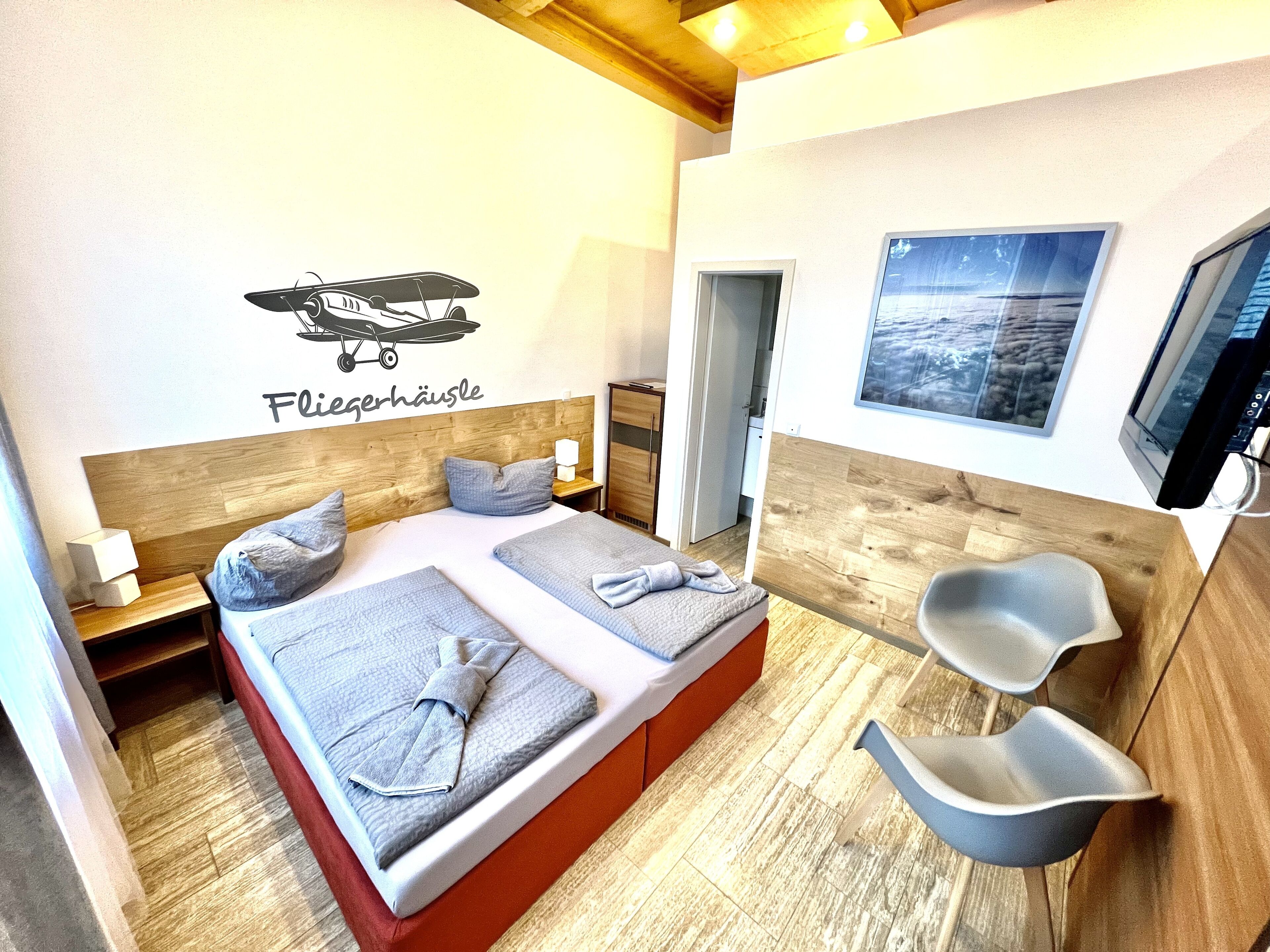 Habitación de hotel con cama, dos mesitas de noche, televisor montado en la pared y ventana con vistas.
