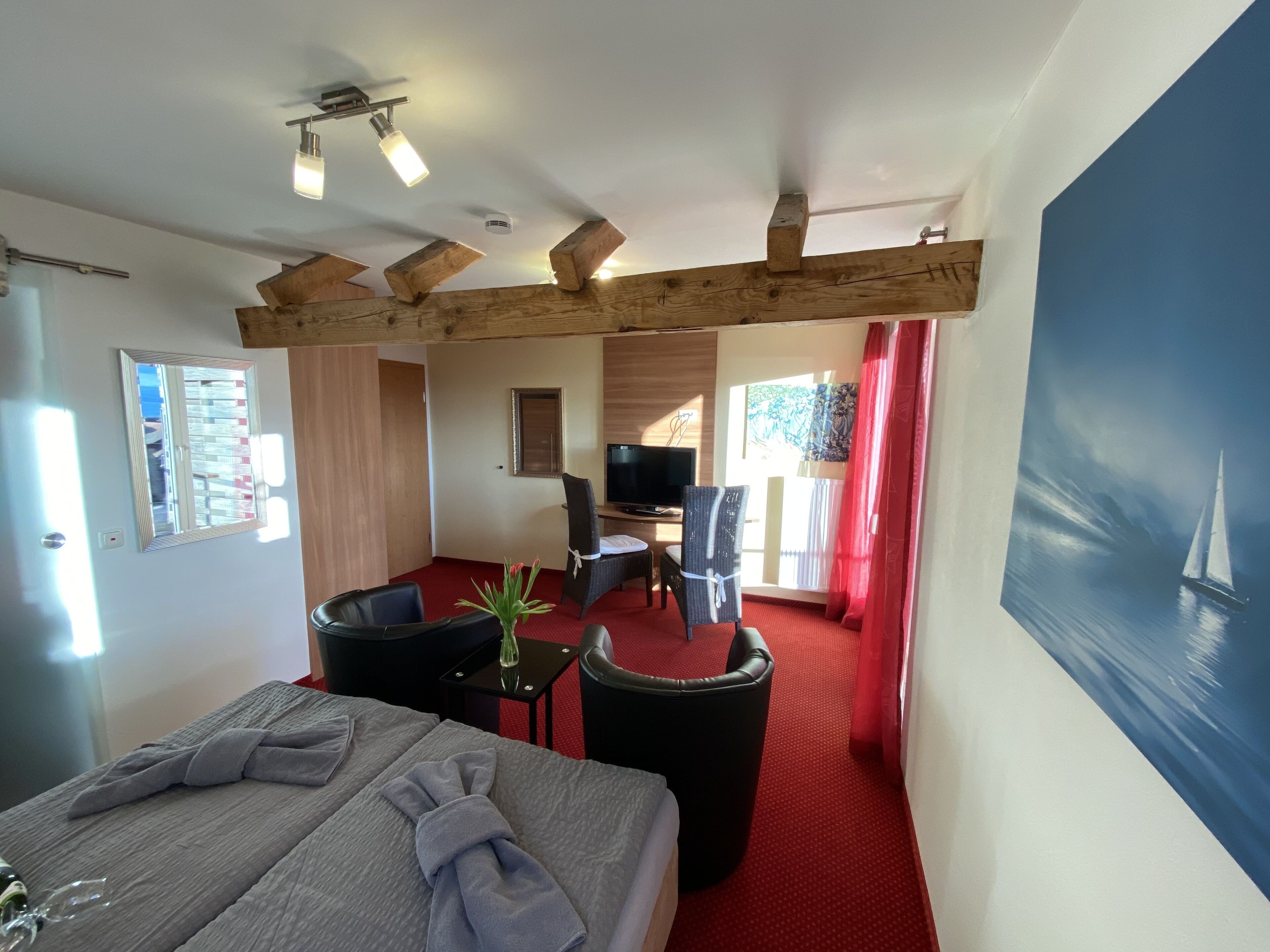 Una habitación de hotel con cama, escritorio, silla, televisión y un cuadro de un velero.