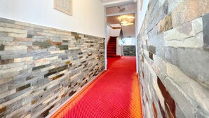 A hallway with a red carpet, stone walls, and a staircase leading to another room.