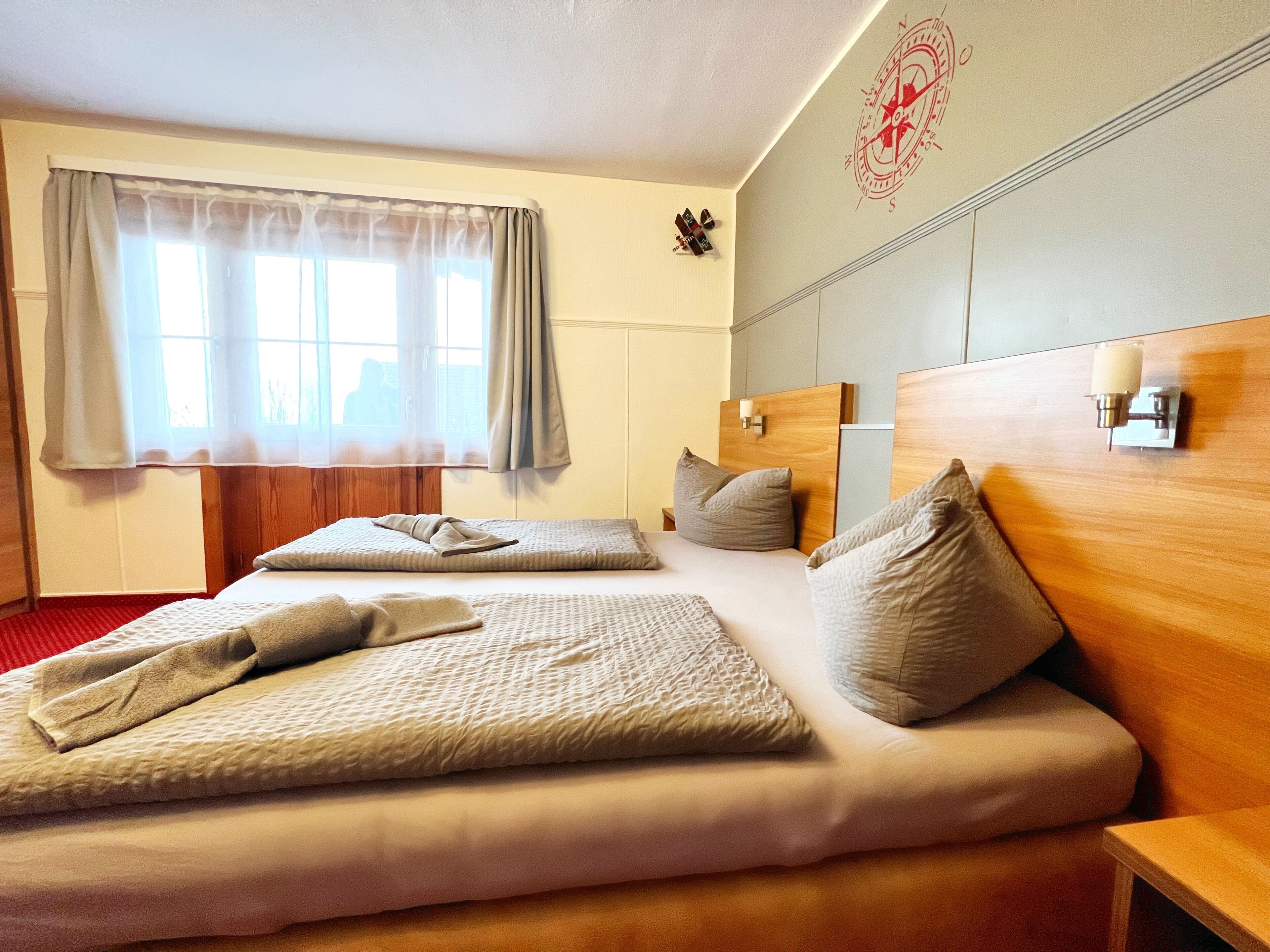 Una camera d'albergo con un letto grande, due comodini, una finestra con tende e una sveglia a muro.