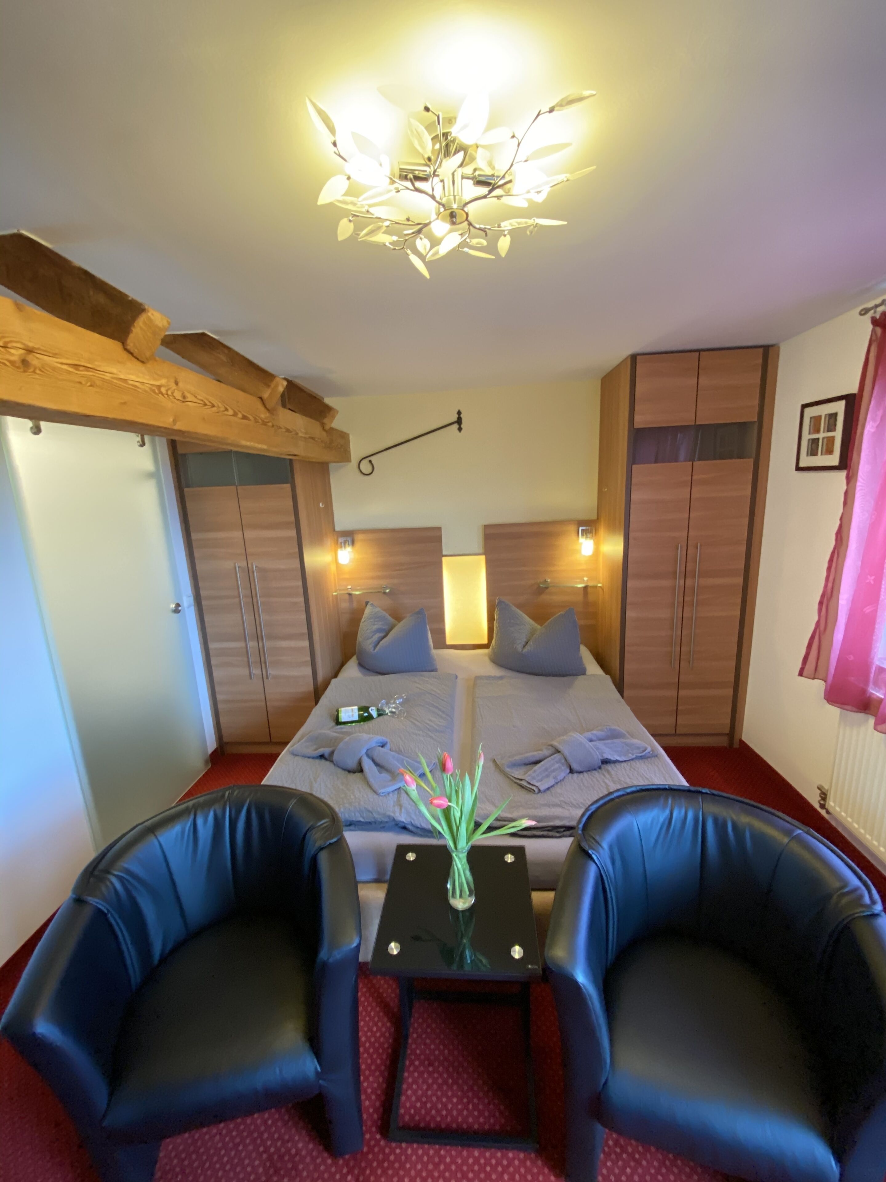 A hotel room with a bed, two chairs, a small table, and a chandelier.