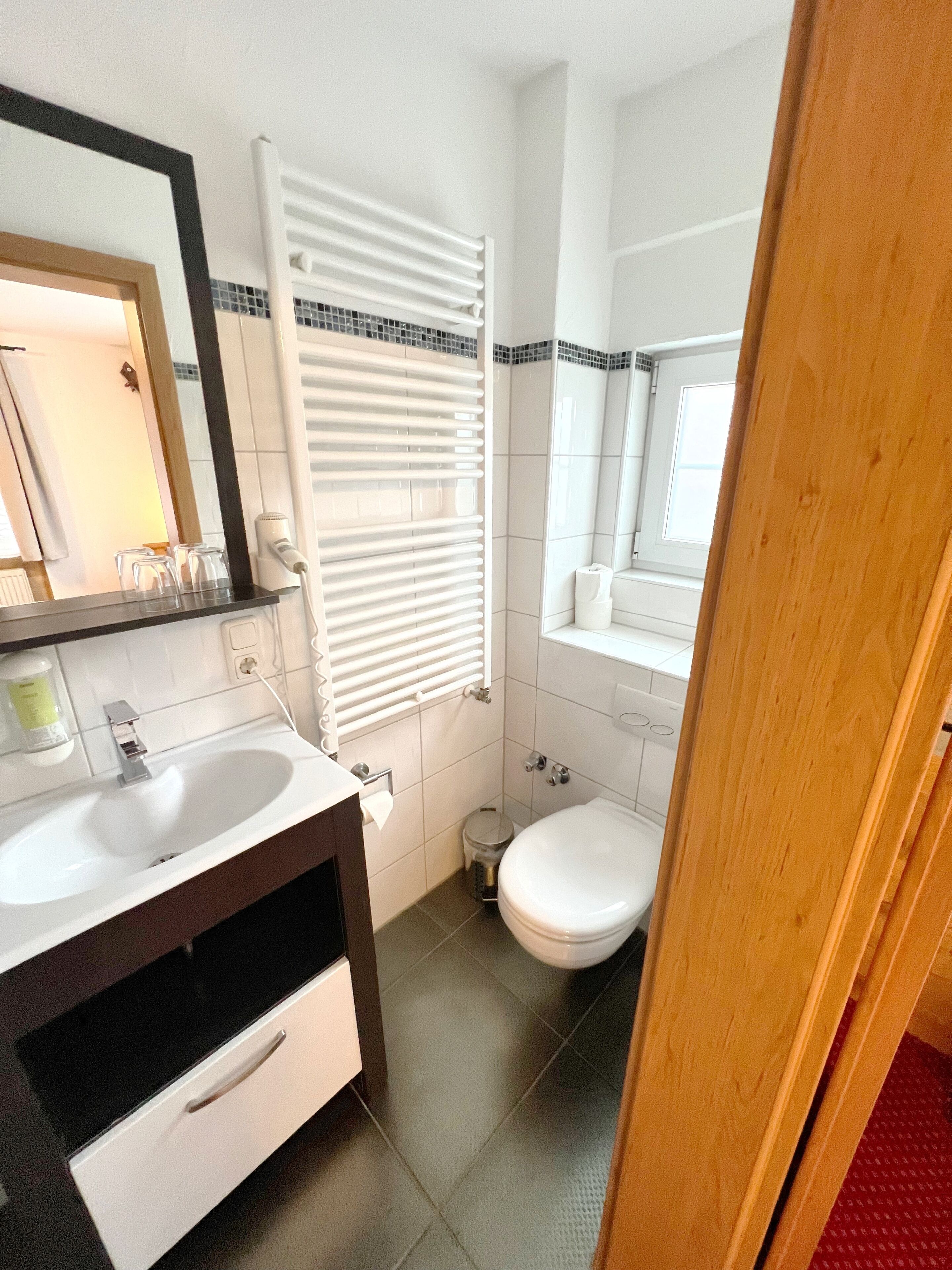 A bathroom with a white sink, a mirror, a toilet, and a window with blinds.
