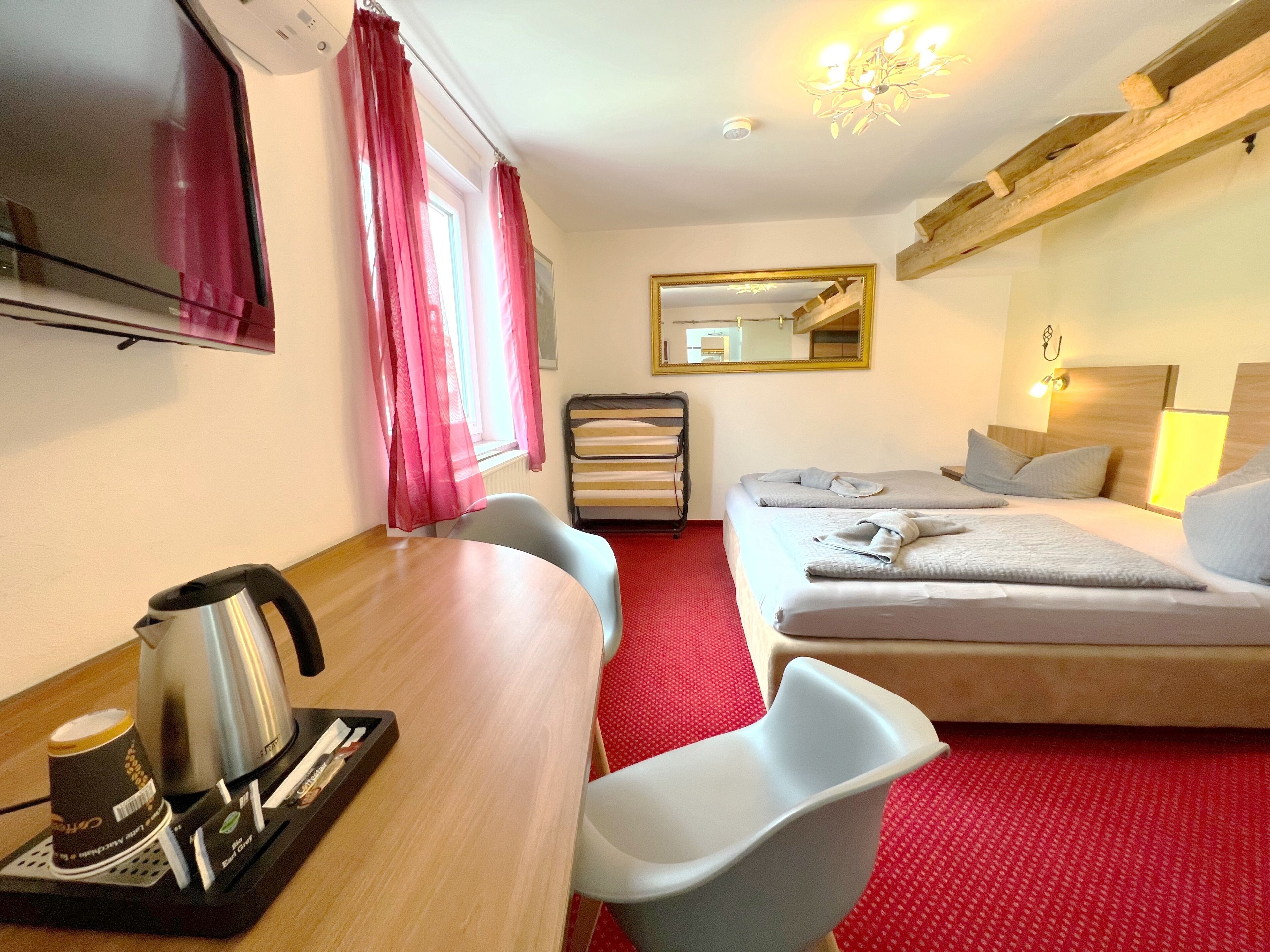 Een hotelkamer met een bed, een bureau met waterkoker, een stoel, een rood tapijt en een spiegel.
