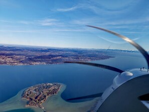 Luchtbeeld van een kustgebied met een klein eiland, een uitgestrekt wateroppervlak en een heldere lucht.