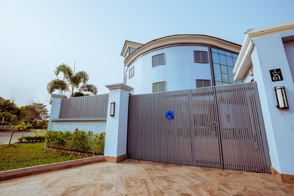 A gated entrance to a modern building with a curved facade, a blue sign, and a well-maintained lawn. - Medallion Hospitality (Lekki)
