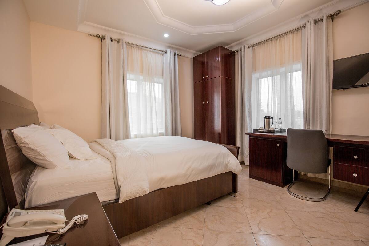 A hotel room with a bed, desk, chair, and a TV mounted on the wall.