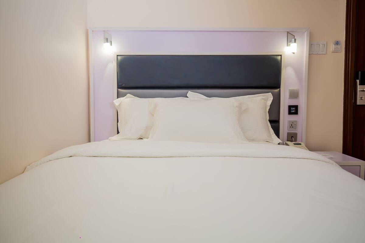 A neatly made bed with white bedding, a dark headboard, and bedside controls.