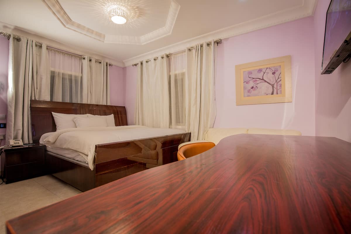 A hotel room with a wooden bed, a desk, a chair, a nightstand, and a painting on the wall.