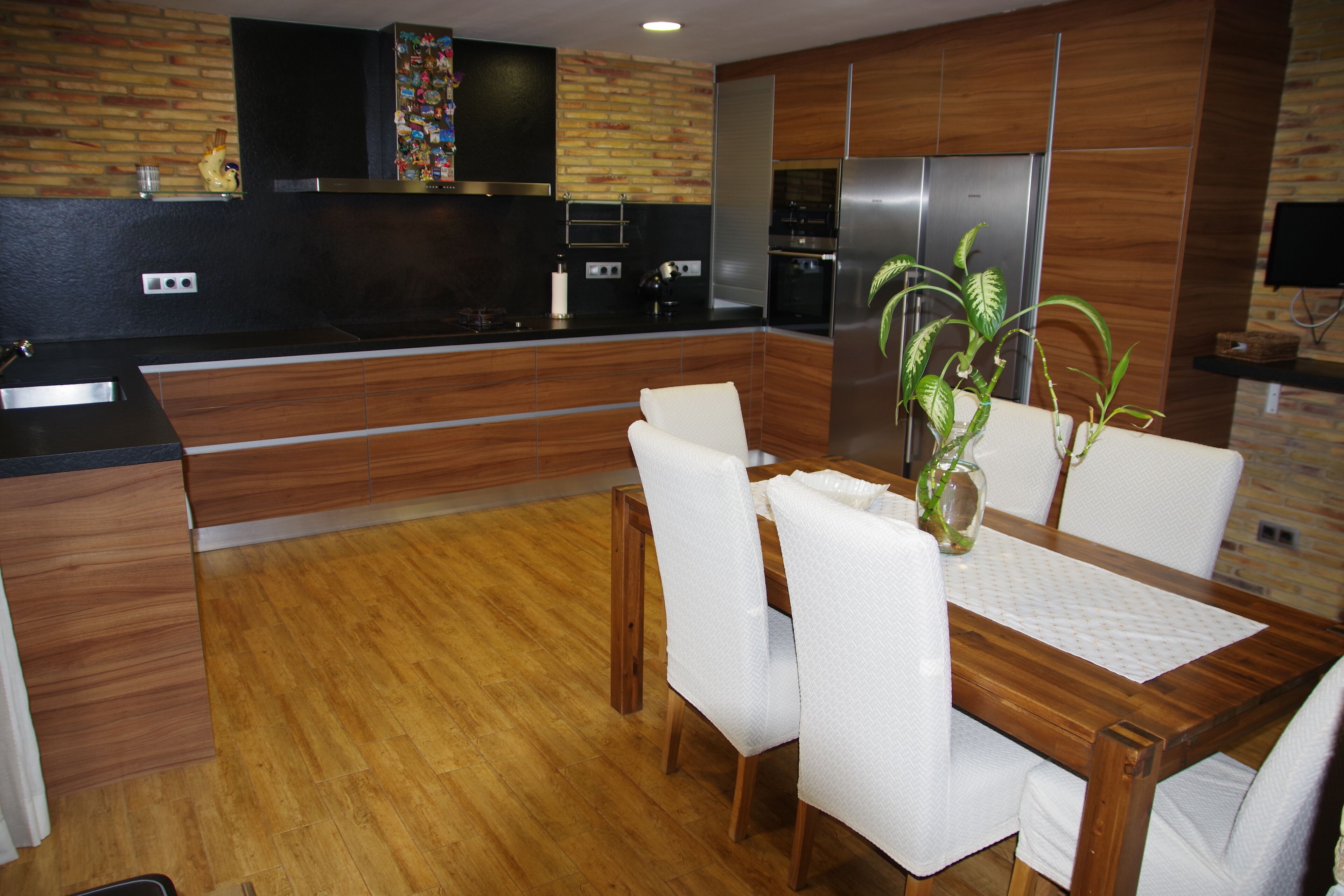 Une cuisine moderne avec des meubles en bois, une cuisinière encastrée et un coin repas comprenant une table en bois et des chaises blanches.