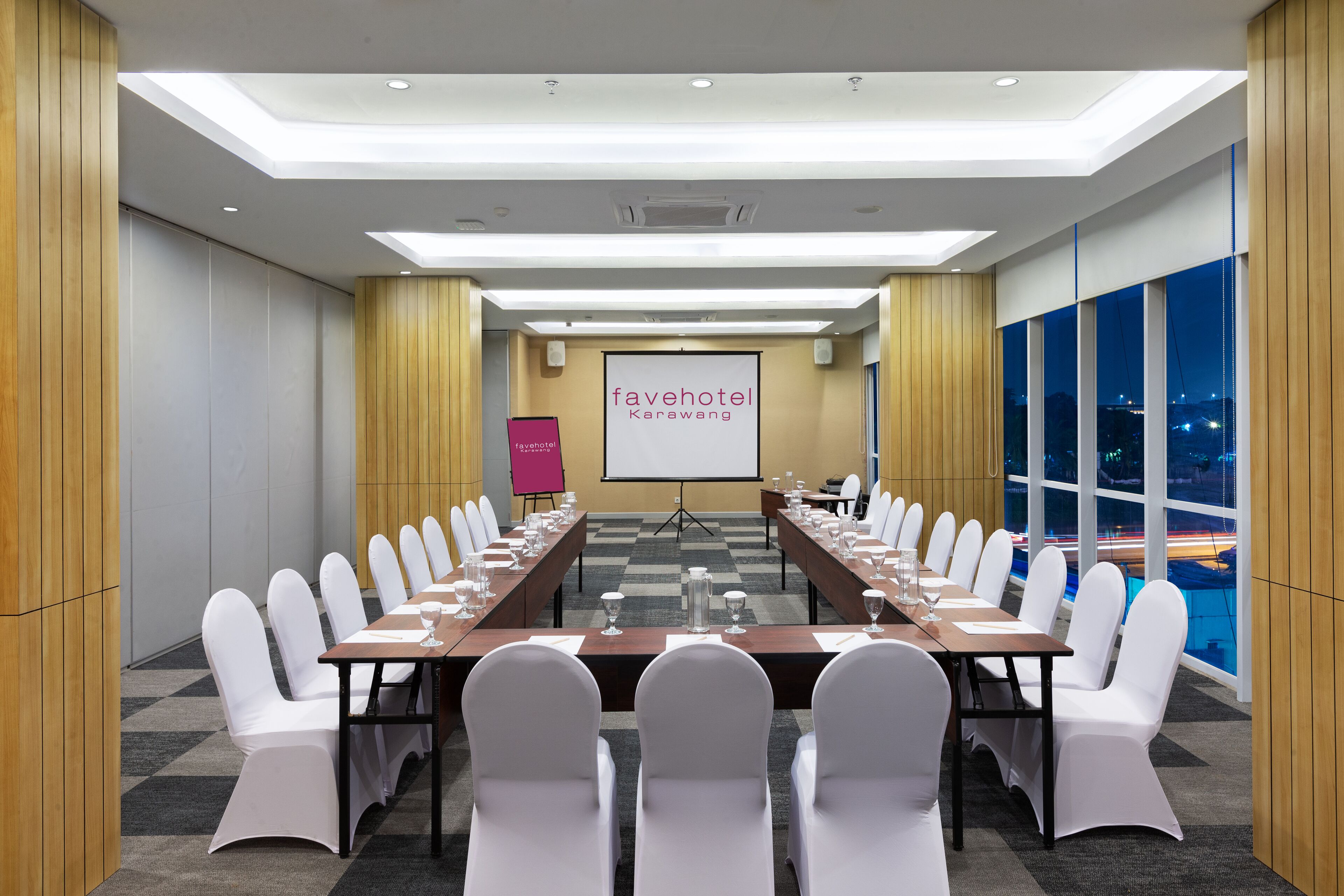 A conference room with a long table, white chairs, and a large screen.