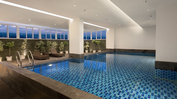 An indoor swimming pool with clear blue tiles, surrounded by white walls and large windows.