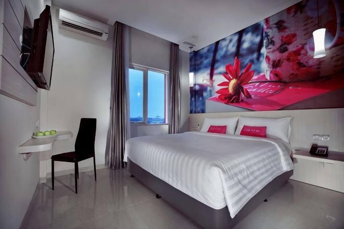 Habitación de hotel con una cama, una silla, un escritorio, un lavamanos y un ventanal grande.