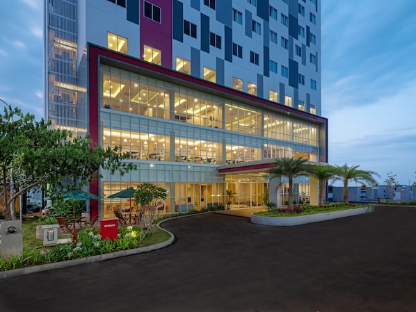 A modern hotel with a glass facade, outdoor seating, and a landscaped entrance.