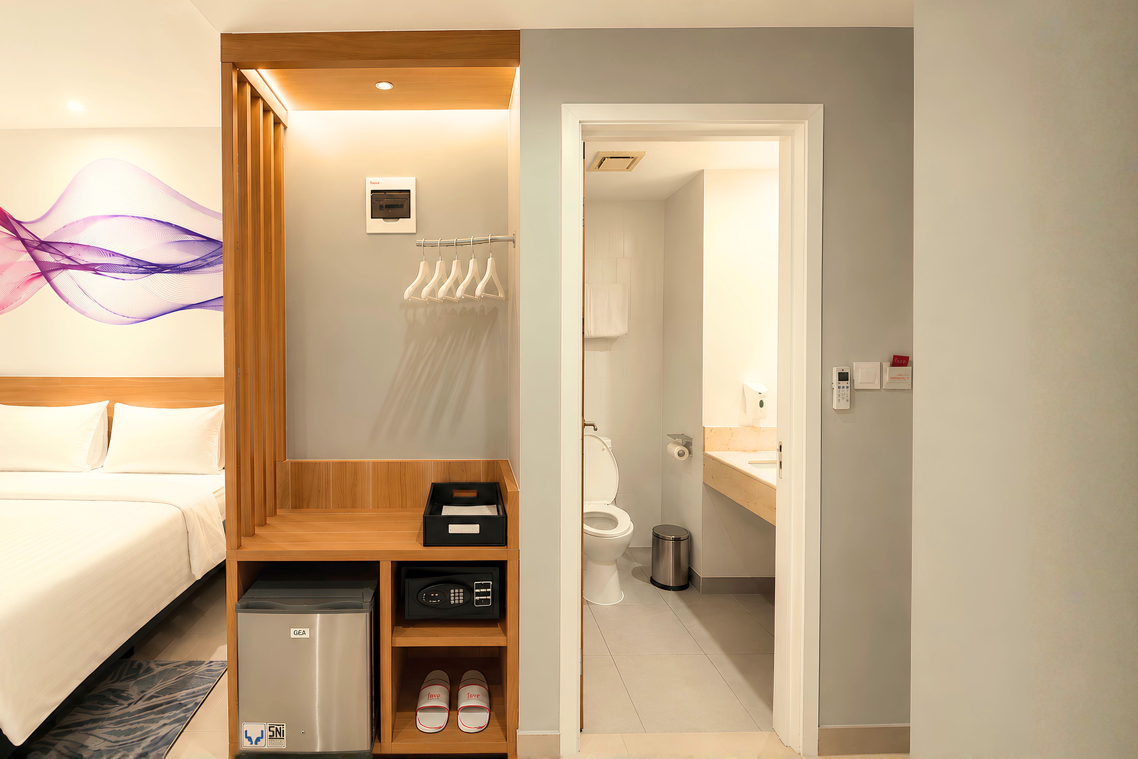 A hotel room with a bed, a wooden storage unit, a shoe rack, and a bathroom with a toilet and sink.