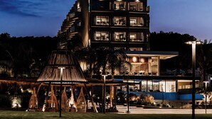 Un edificio moderno de varios pisos con una terraza en la azotea y un área de estar exterior bien iluminada.
