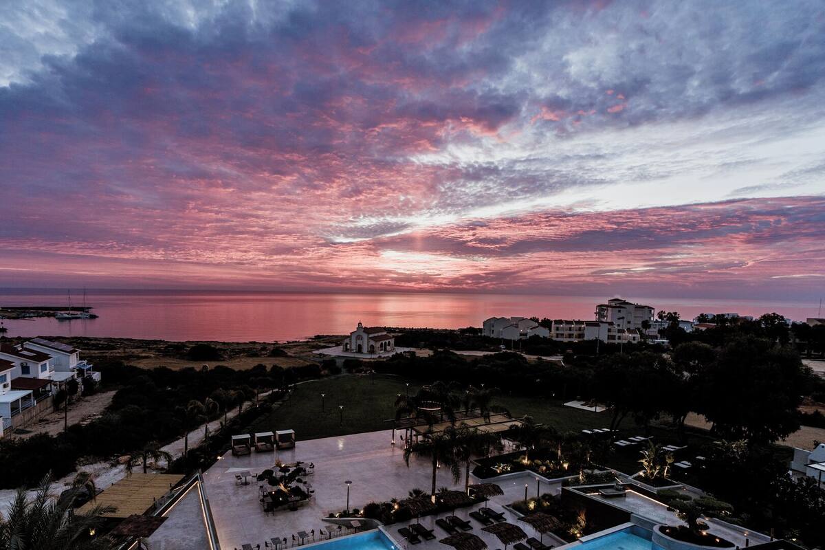 Ein Resort mit Poolbereich, Liegestühlen und Blick auf den Sonnenuntergang über dem Meer.