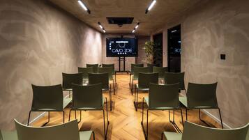 A conference room with a large screen, wooden floor, and green chairs arranged in rows.