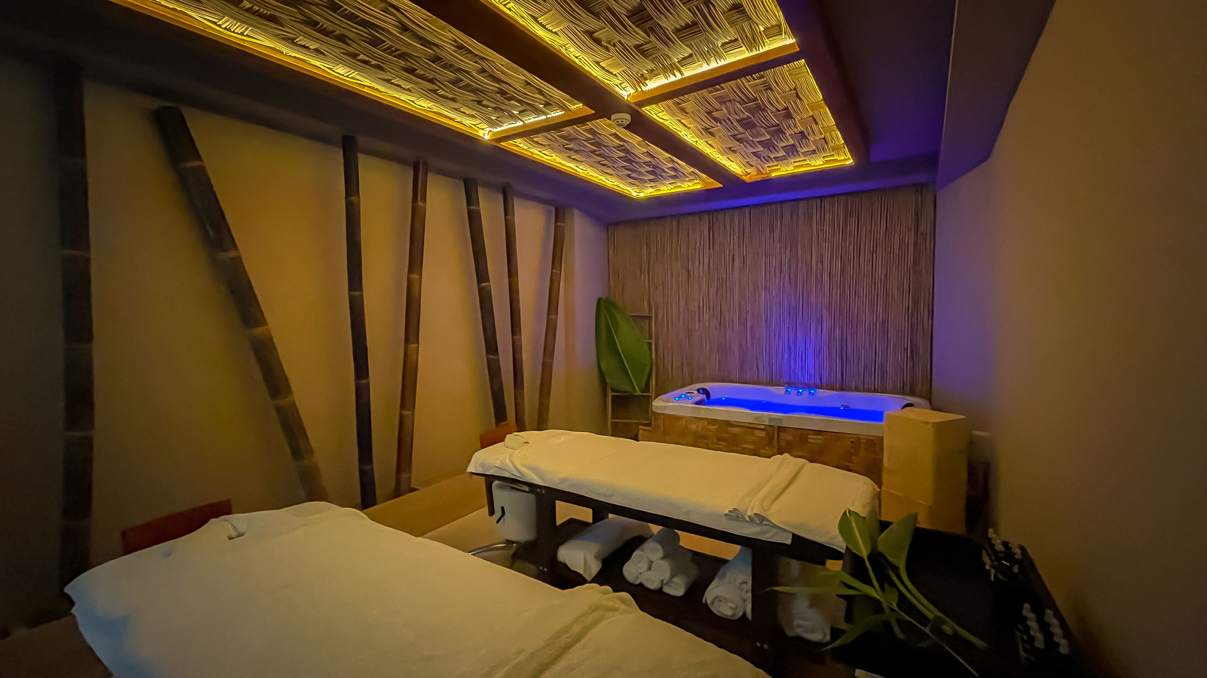 A spa room with a massage table, a hot tub, and a wooden wall with a woven ceiling design.