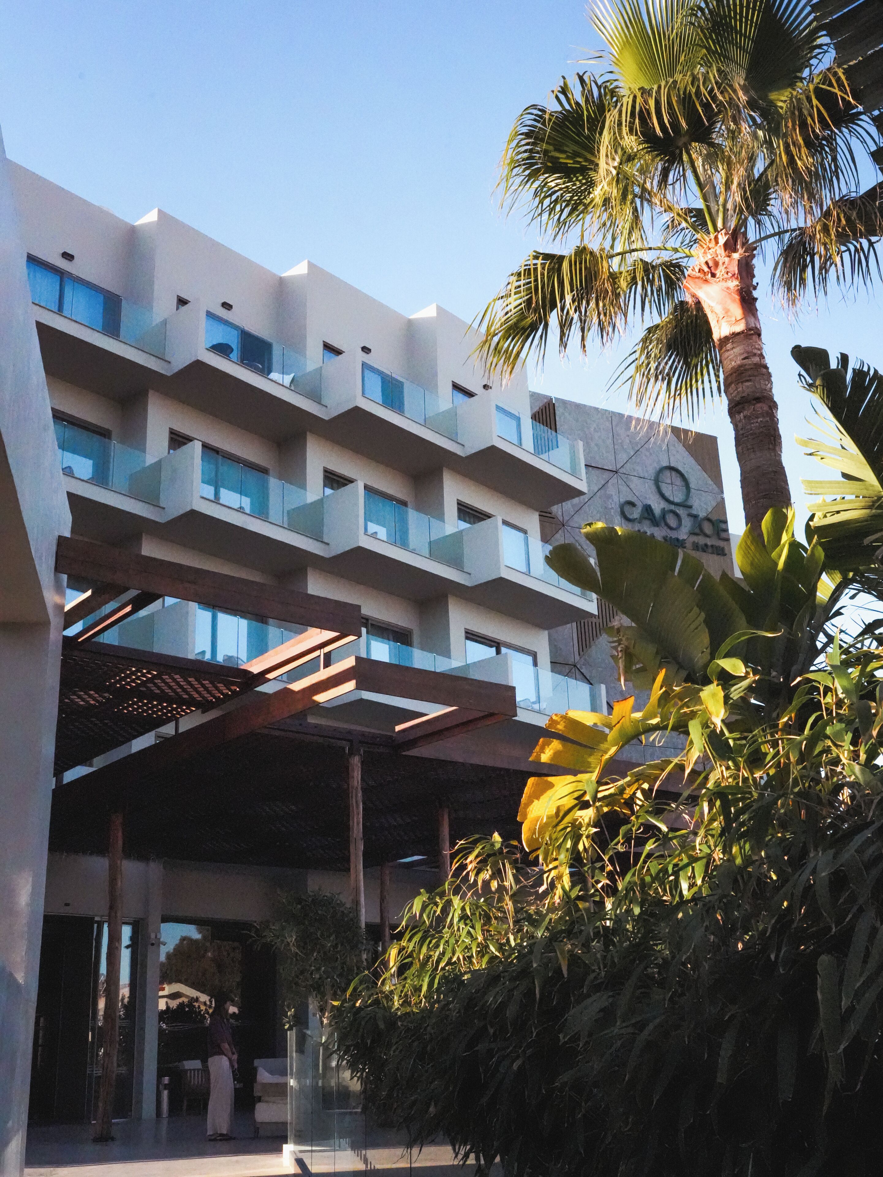 A multi-story hotel with balconies, a covered entrance, and tropical vegetation.