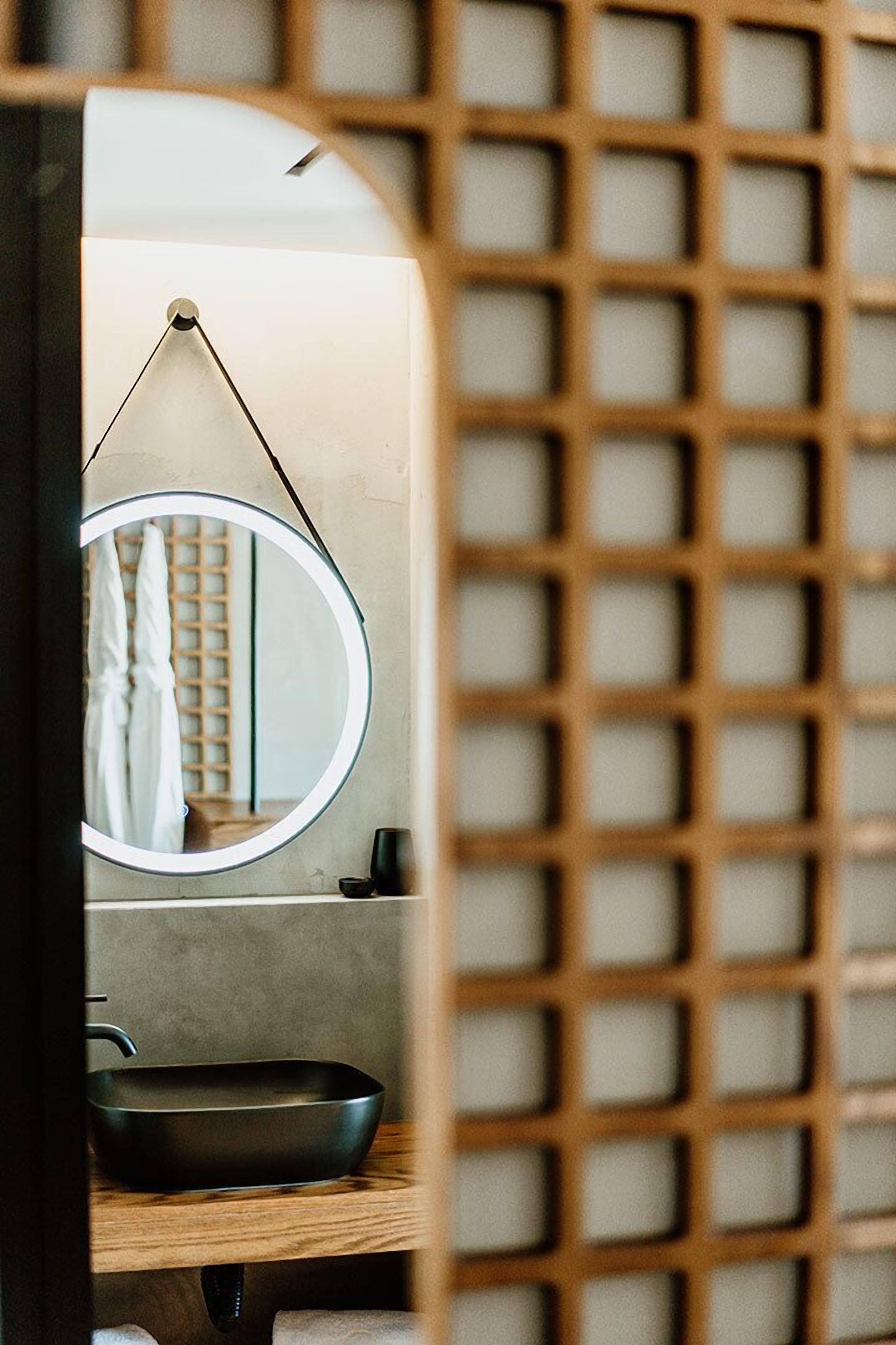 Een badkamer met een ronde spiegel, een zwart wastafel en een houten plank.
