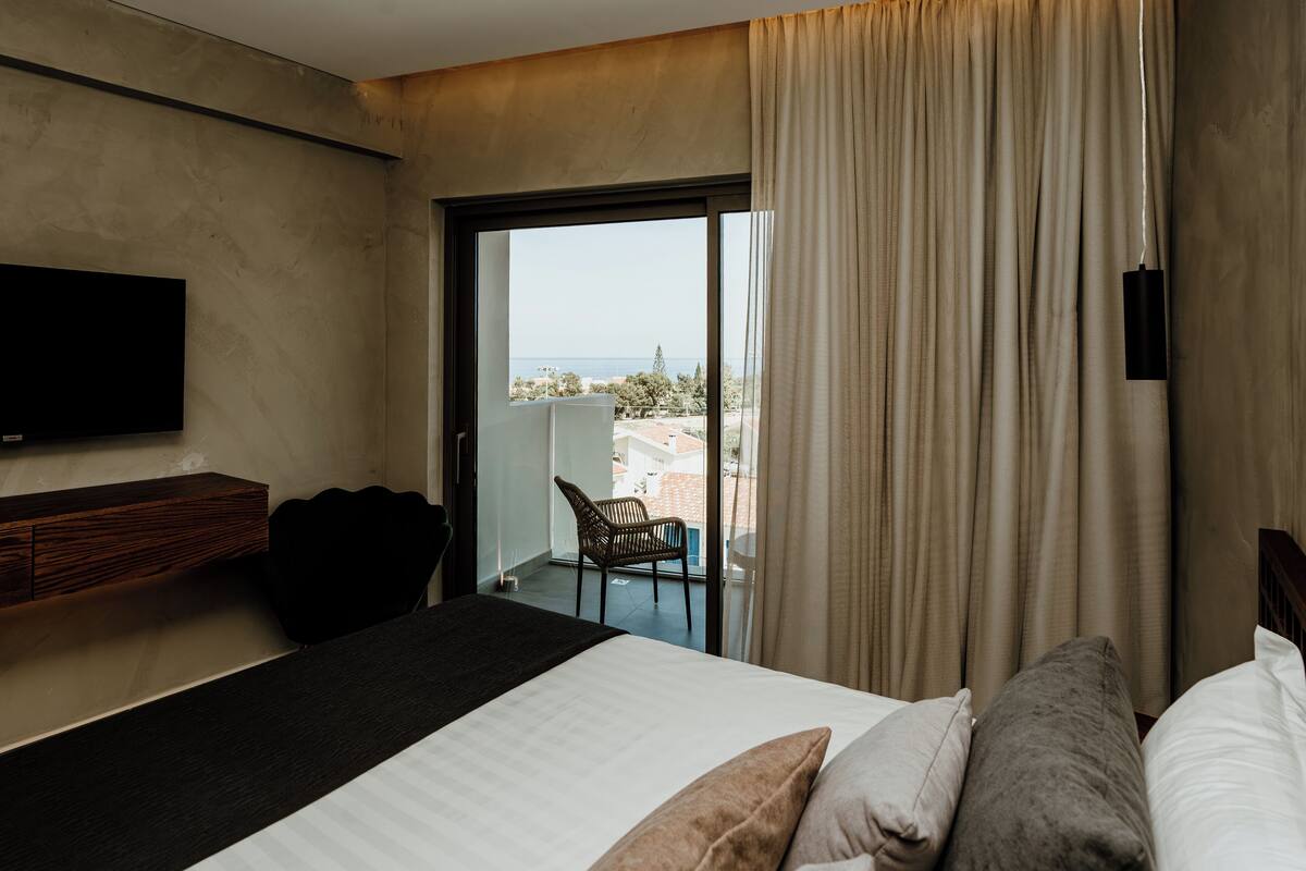 Ein Hotelzimmer mit Bett, Wandfernseher, Sessel und Meerblick durch eine Schiebetür.