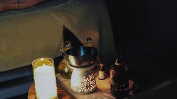 A dimly lit room with a bed, a candle, a lantern, and a bottle on a wooden tray.