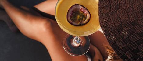 Eine Person hält ein Glas mit einem Getränk, trägt ein weißes Oberteil und ein braunes Strickteil.