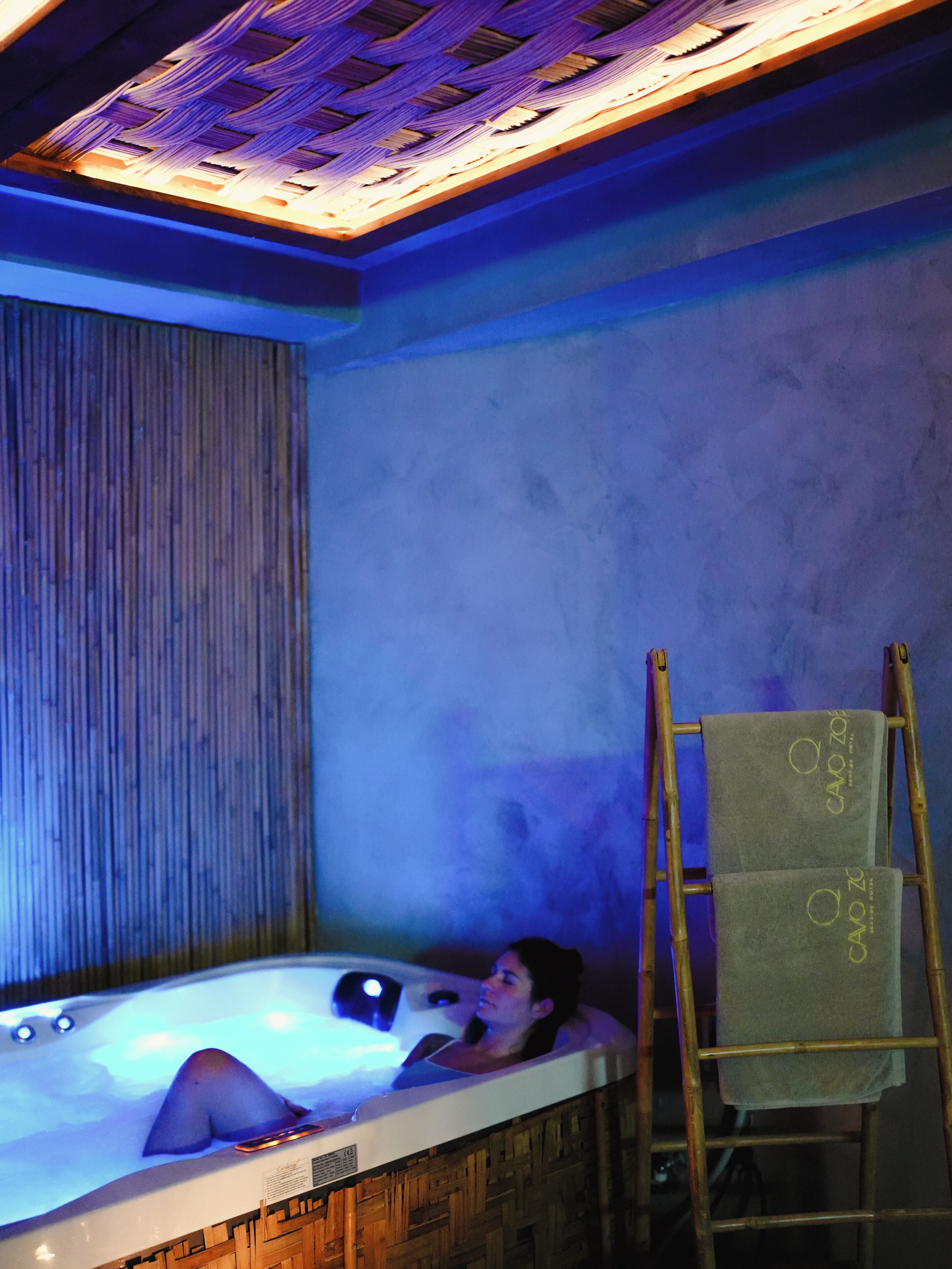 Una persona relajándose en un jacuzzi con una escalera de madera y toallas.