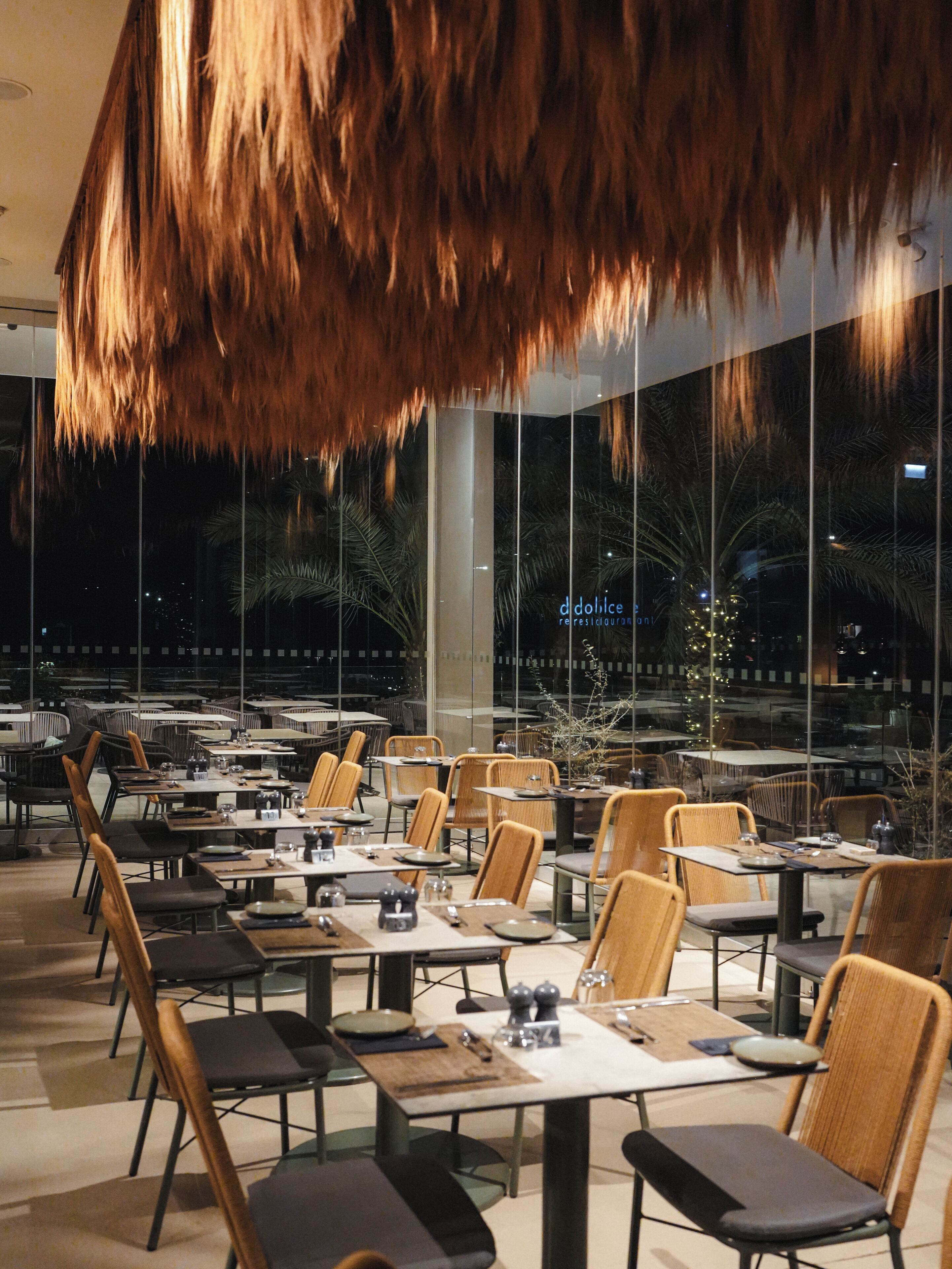 Un espace de restauration intérieur avec des tables et des chaises, de grandes fenêtres et un luminaire suspendu.