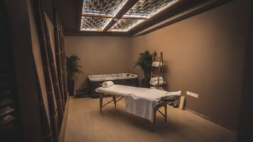 A spa room with a massage table, a hot tub, and a ceiling skylight.